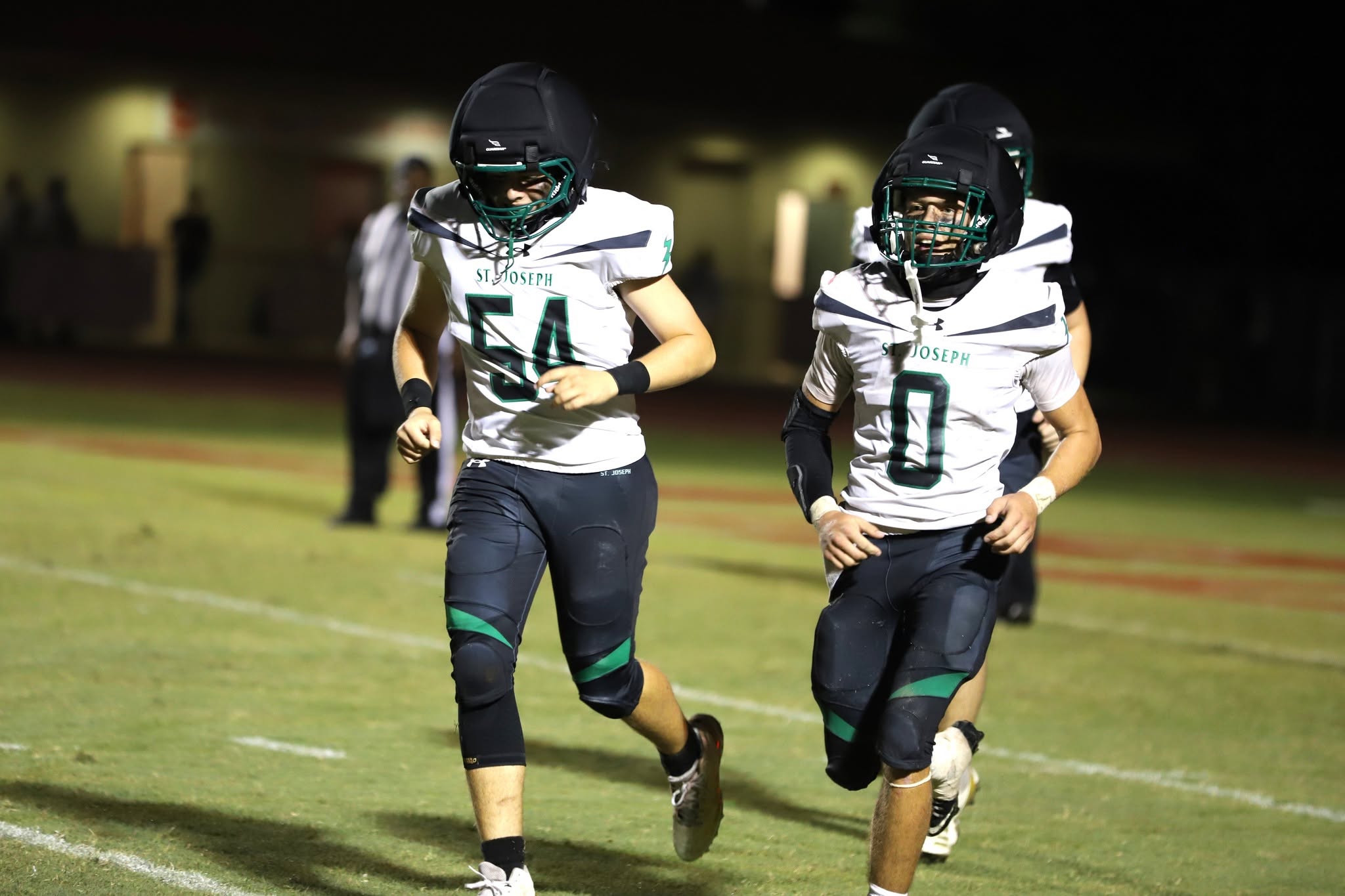 SJA Flashes football teammates in white jerseys running on the field.